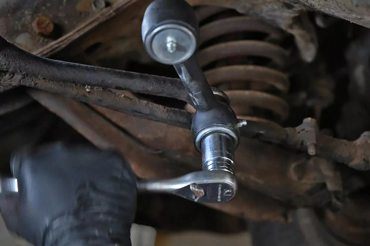 A mechanic wearing a black nitrile glove tightens the idler arm down with a socket wrench.