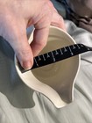 Hand measuring the interior diameter of a white ceramic bowl with black floral print, using a dark diagonal ruler for scale.