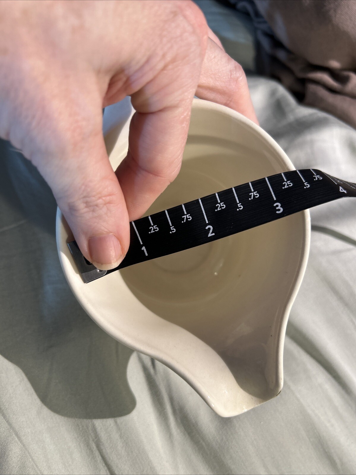 Hand measuring the interior diameter of a white ceramic bowl with black floral print, using a dark diagonal ruler for scale.