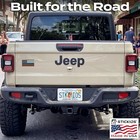 Tan Jeep Wrangler back bumper with black American flag sticker and “Built for the Road” text.