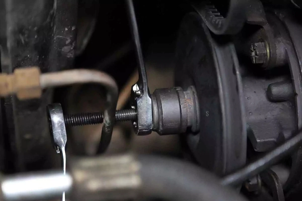 A mechanic reinstalls the pulley on the power steering pump using a pulley tool and two box wrenches.