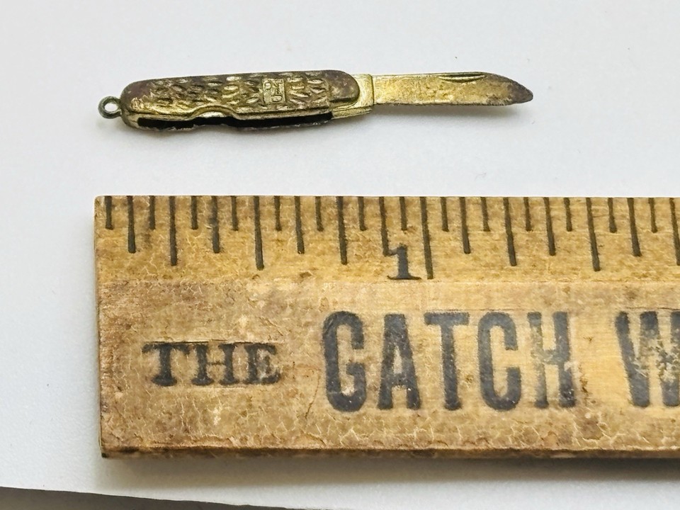 A tiny folding pocket knife rendered as a gold-tone bracelet charm — the kind of miniature novelty that stops people mid-sentence.