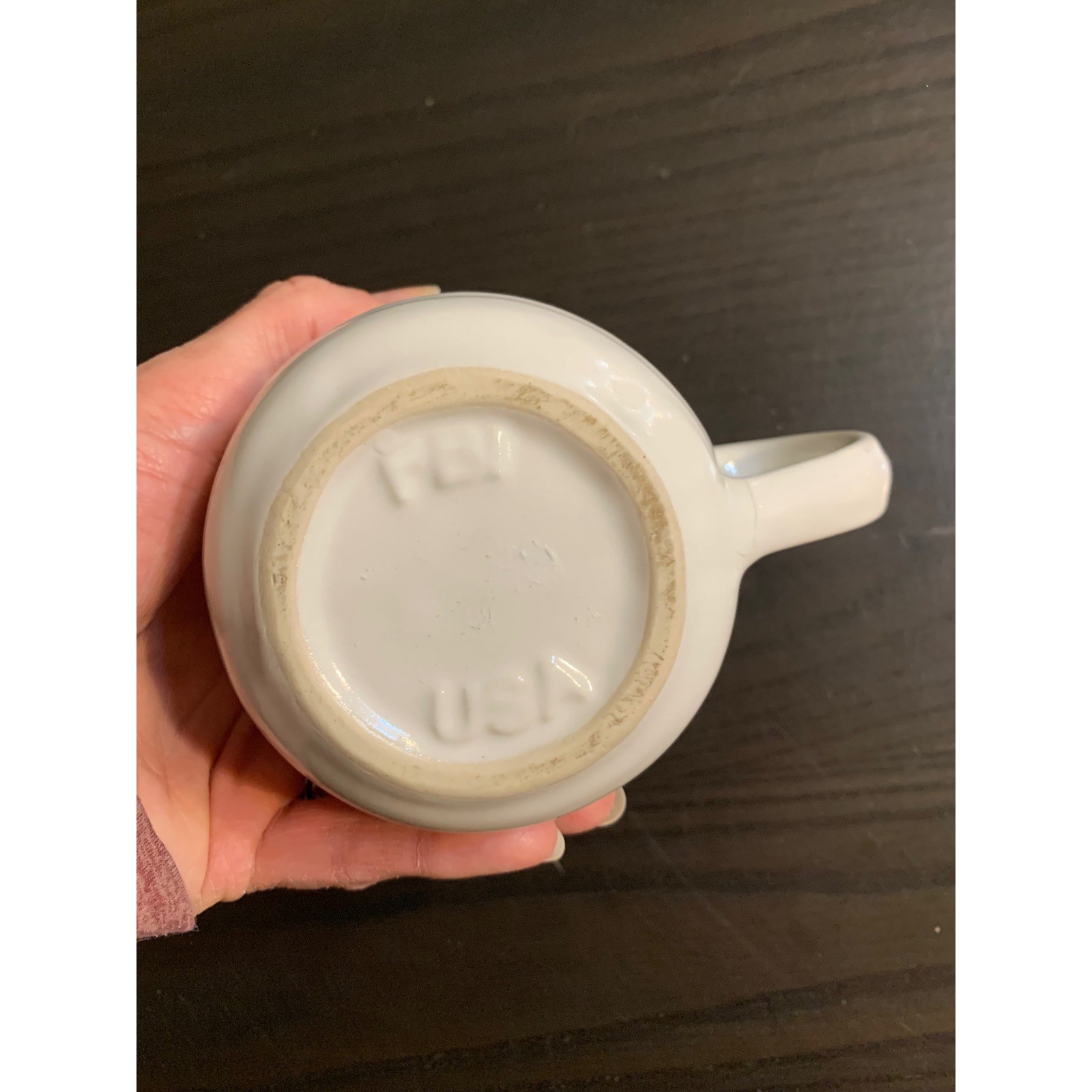 White ceramic coffee mug with ribbed beehiive pattern, tan logo on dark base, held in hand against dark background.