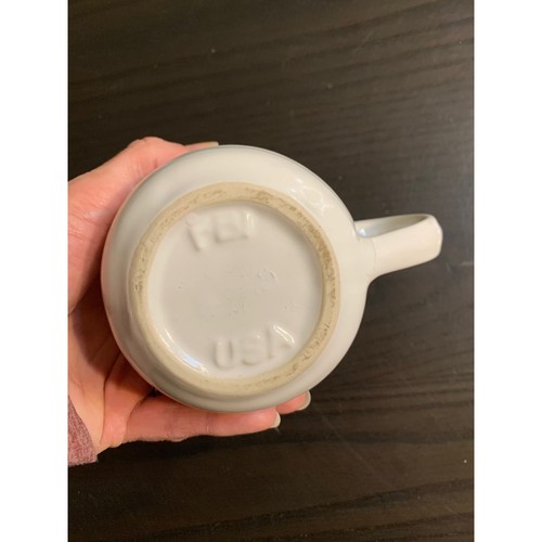 White ceramic coffee mug with ribbed beehiive pattern, tan logo on dark base, held in hand against dark background.