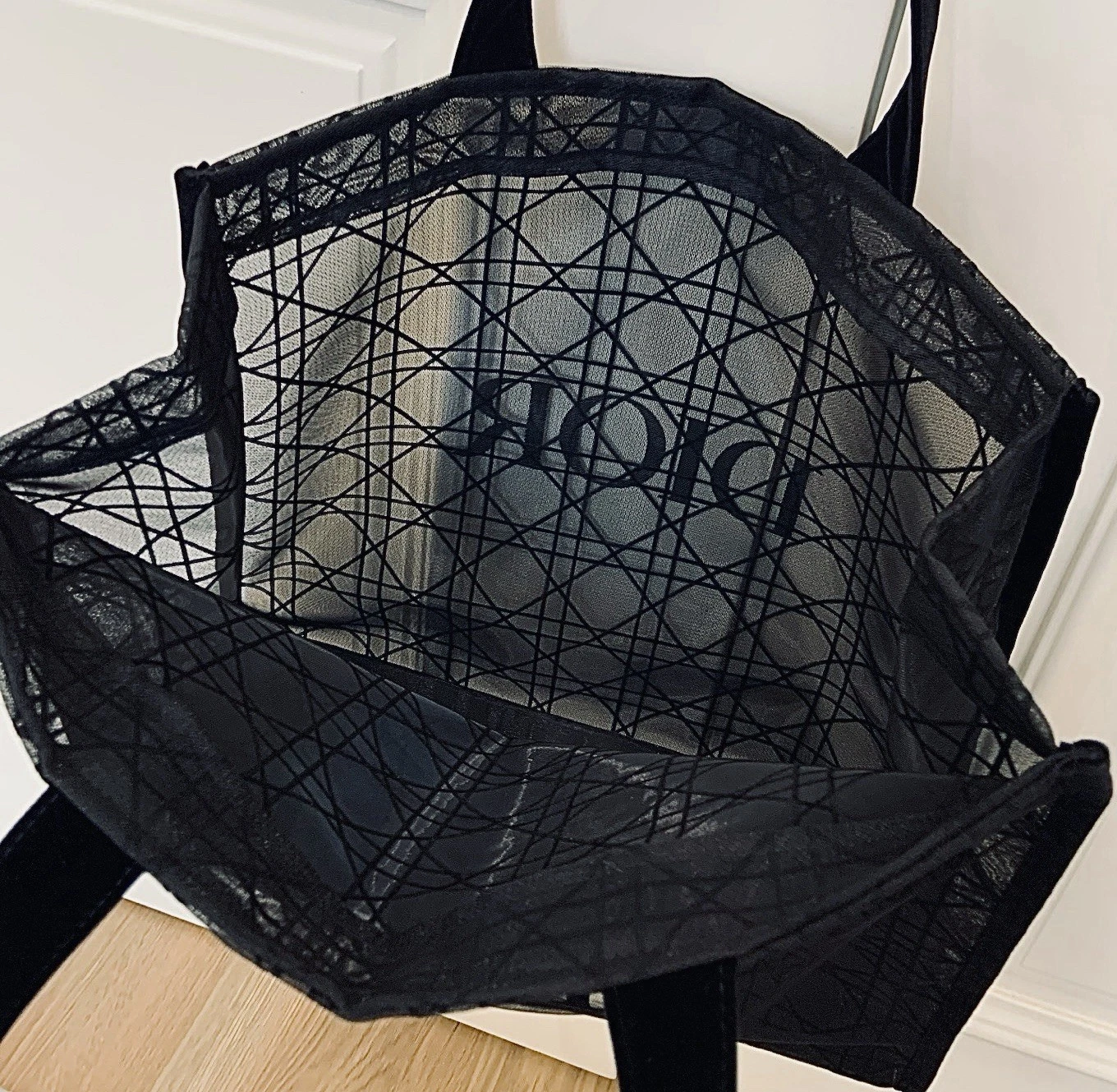 Black lace mesh tote with geometric pattern and �DIORBEAUTY� logo, displayed on a wooden surface.