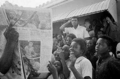 Cassius Clay reading newspaper report of his fight while outside w - Old Photo