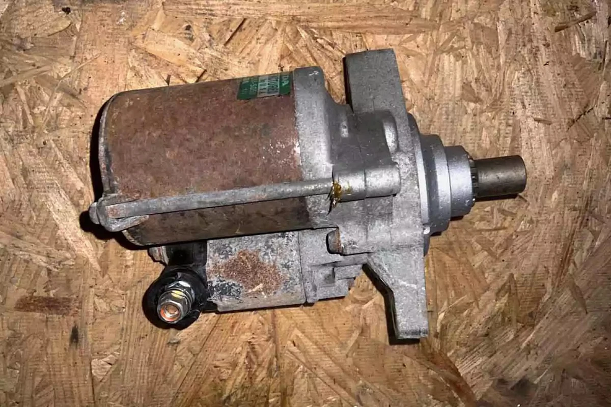 A rusty used OEM starter motor for the 2001-2005 Honda Civic, displayed on a particle board background.