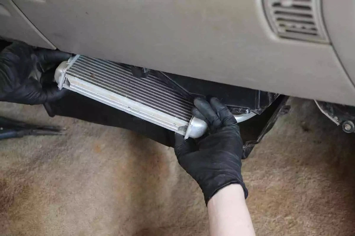A mechanic wearing a black glove pulls the heater core out through the HVAC box.