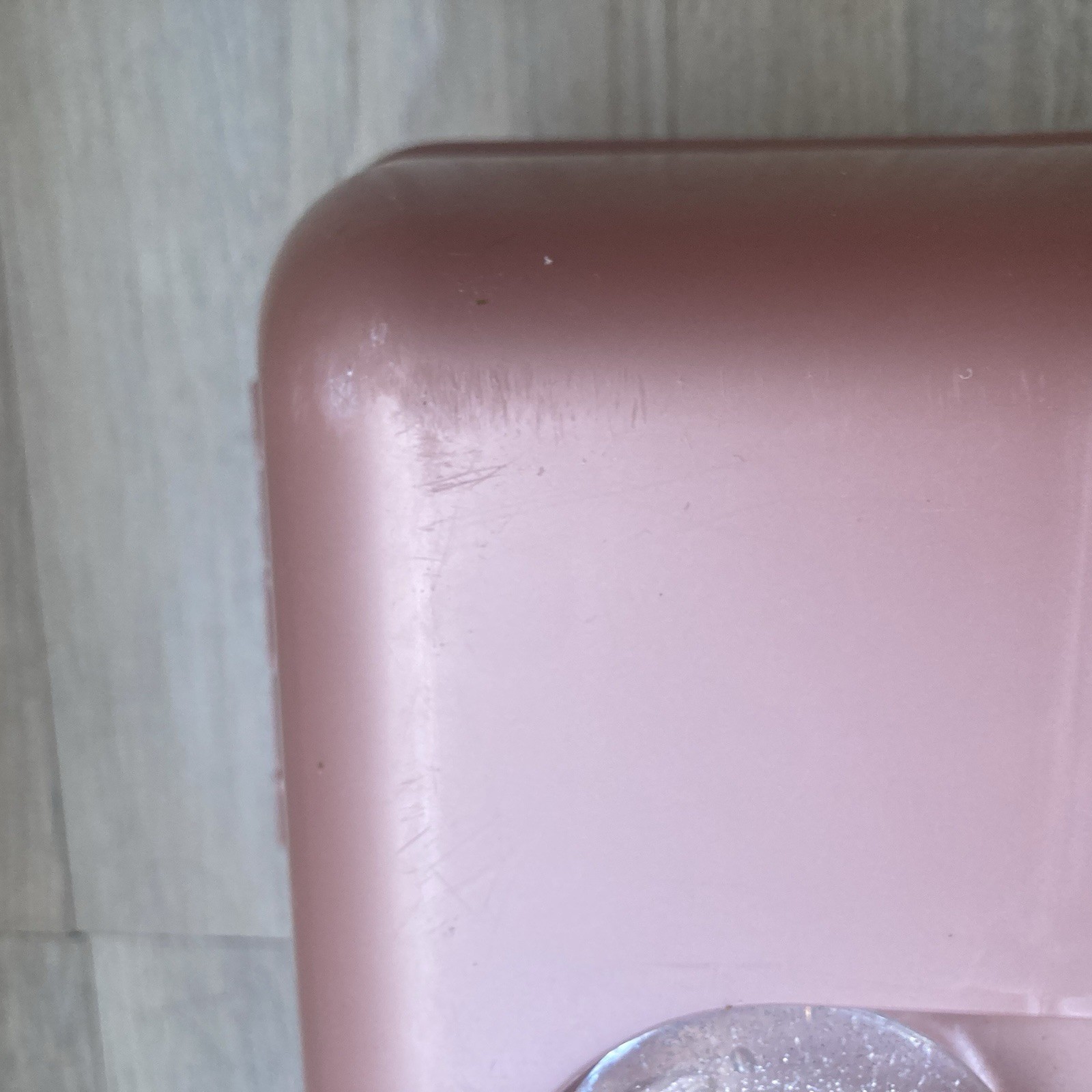 Pink rectangular Caboodle makeup box with visible scratches and textured edges against a white tile background.