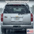 Silver Chevrolet Suburban with American flag sticker, rain-soaked rear window, and “STK IO” plates.