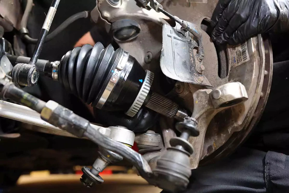 A mechanic pulls the knuckle outward in order to slide the axle drive end into the wheel hub.