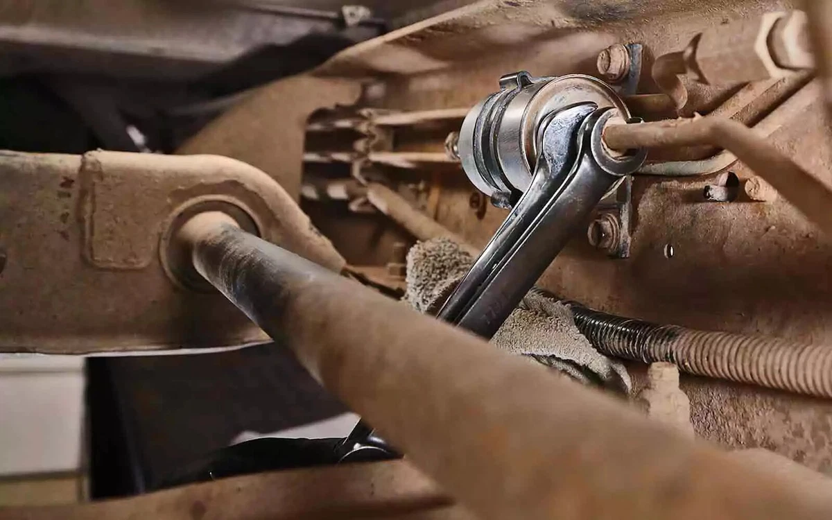 A mechanic using two open-end wrenches to remove a fuel filter. A shop towel is placed beneath the filter to catch any dripping fuel.