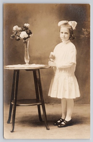 RPPC Young Girl White Bow Posing Next to Table Flowers Identified CYKO Postcard - Picture 1 of 2