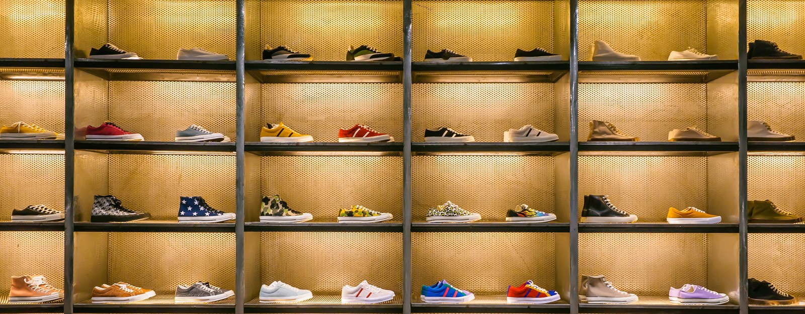 Eine Ausstellung verschiedener Sneaker auf Regalen, die unterschiedliche Farben und Designs vor einem warmen, beleuchteten Hintergrund präsentieren.