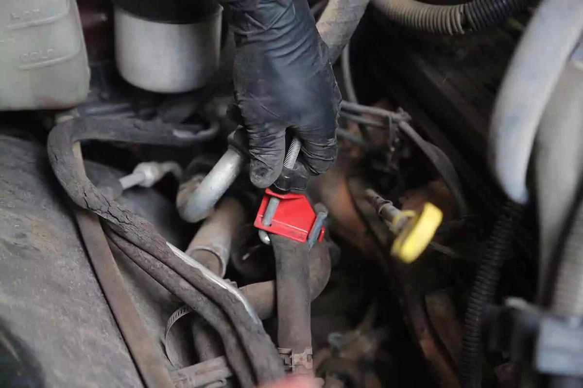 A mechanic wearing a black glove clamps a heater hose.