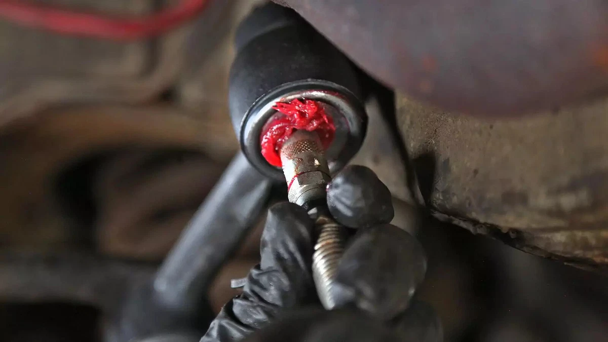 A mechanic wearing a black nitrile glove greases a replacement idler arm.
