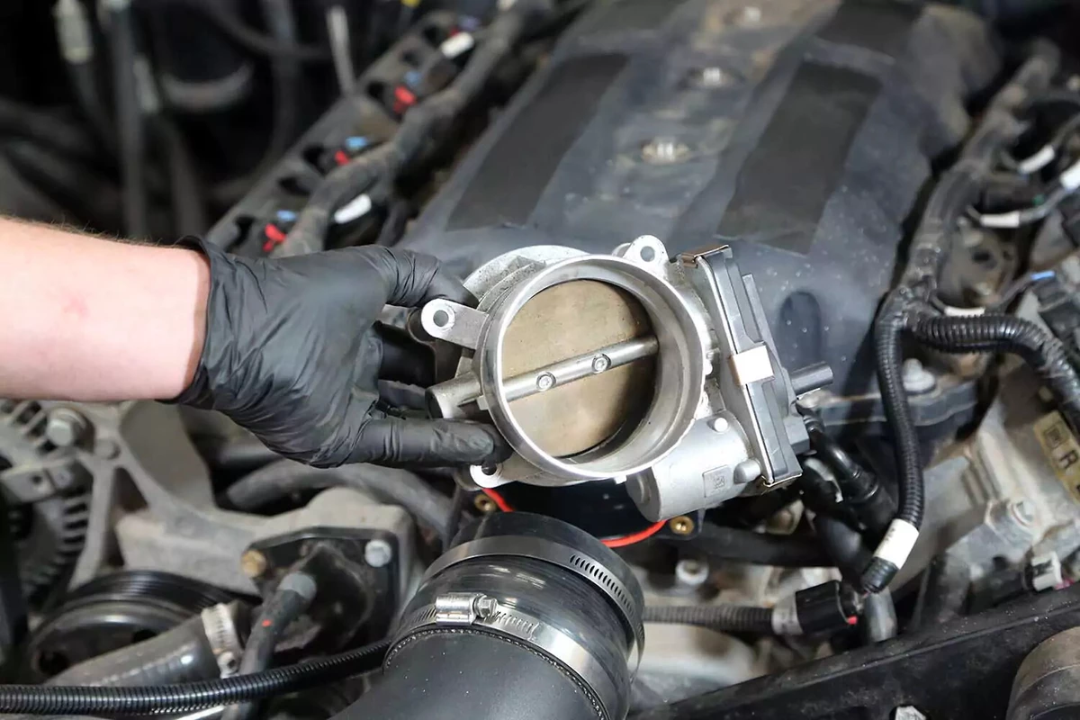 A mechanic removes the throttle body from the intake manifold.