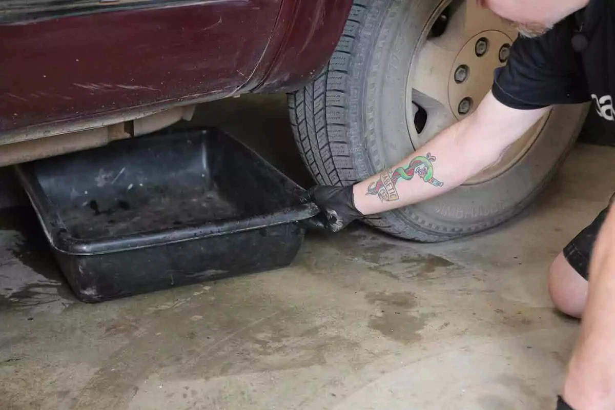 A mechanic places a drain pan in position beneath a car.