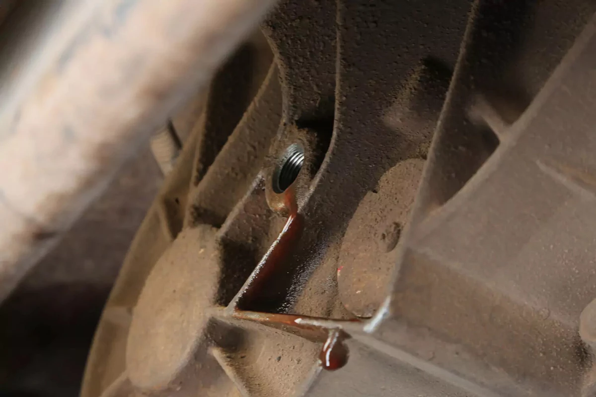 A transfer case with the fill port open and some new transfer case fluid leaking out of it.