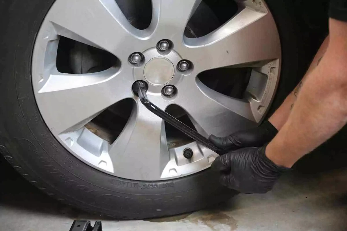 A mechanic wearing black gloves uses a tire iron to loosen the lug nuts on a vehicle's tire.