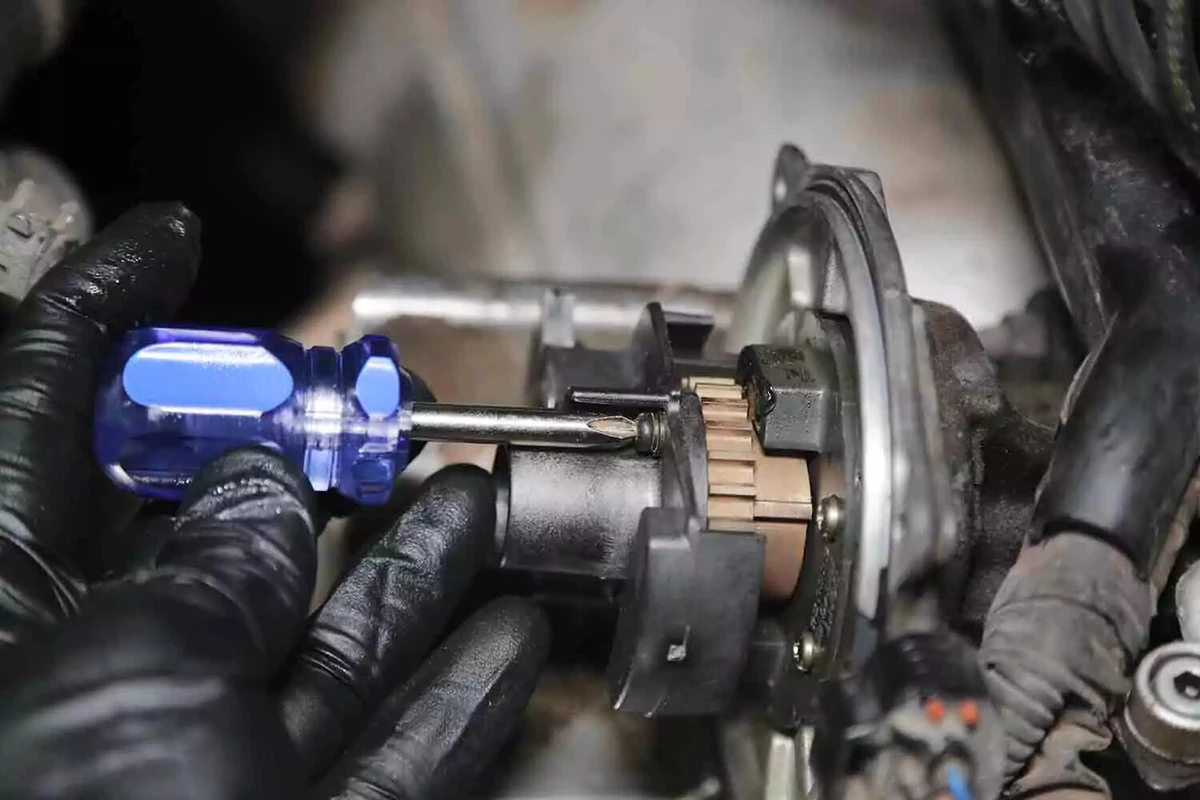 A mechanic wearing black gloves uses a screwdriver to install a new rotor in a vehicle.