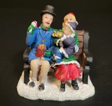 St. Nicholas Square Christmas Village Family Sitting On Park Bench