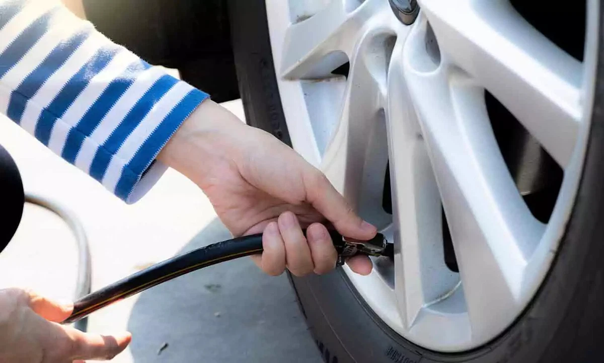 A driver wearing a white and blue striped shirt adds air to a tire at a service station.
