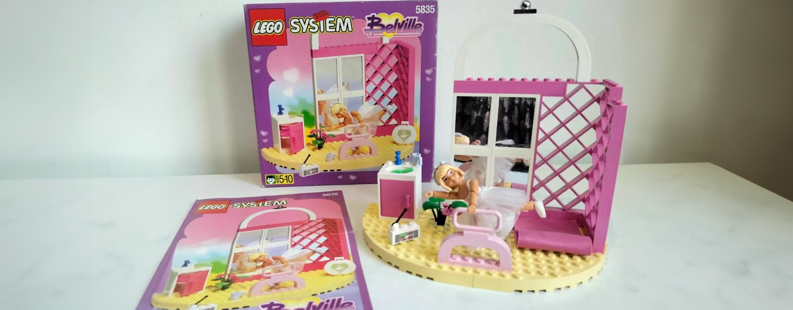 Aufnahme von einem „LEGO Belville”-Set, das auf einem weißen Untergrund steht. Man sieht ebenfalls eine Bauanleitung sowie die Originalverpackung.