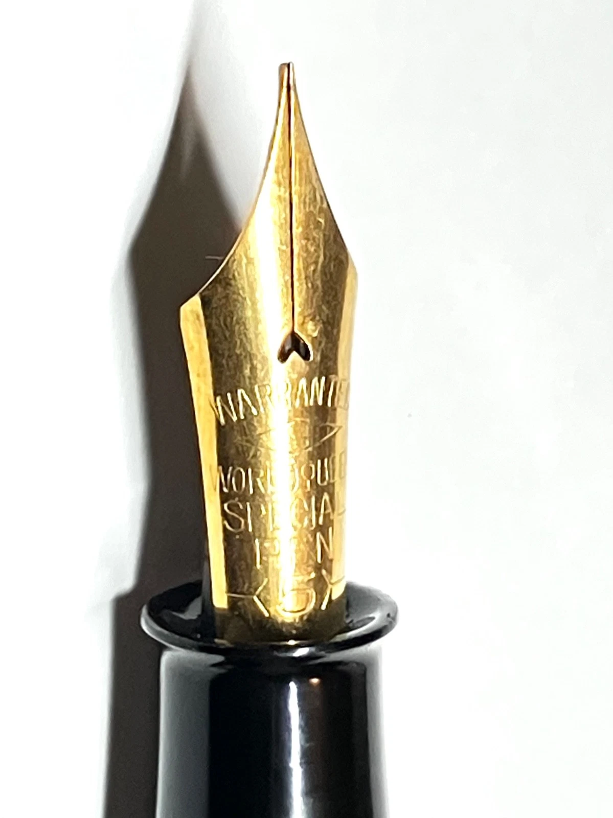 Gold vintage fountain pen with black ink shut off, white body, and gold lettering on a wooden base.