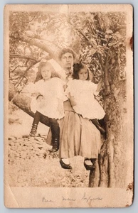 Woman & Two Young Girls in White Dresses with Hair Bows Posing in a Tree RPPC - Picture 1 of 2