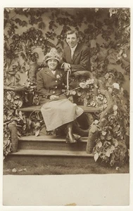 SMILING COUPLE POSE IN A FAUX GARDEN: WHY IS THIS WOMAN HOLDING A WHIP? (RPPC) - Picture 1 of 2