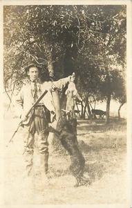 Cazador RPPC con rifle, conejo muerto y perro negro de pie, desconocido EE. UU. - Imagen 1 de 2
