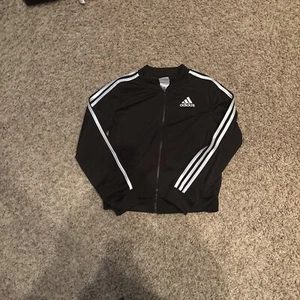 The image shows a black Adidas jacket with white stripes on the sleeves. - Picture 1 of 4