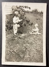b&w photo 2 1/4 x 3 1/4 baby in yard with boy pulling chickens out of his hat