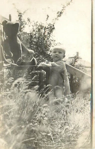 Tarjeta postal RPPC bebé Eileen joven se apoya junto al oso de peluche en silla - Imagen 1 de 2