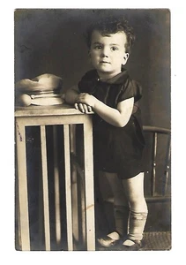 Postal RPPC de principios de 1900, niño pequeño posando en silla con sombrero de servicio - Imagen 1 de 2