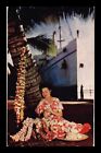 DR JIM STAMPS US WOMAN STRINGING LEI NEXT TO TREE AND BOAT UNPOSTED POSTCARD