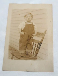 1907-1929 RPPC FOTO POSTKARTE Junge im Overall stehend auf Stuhl draußen NOKO - Bild 1 von 2