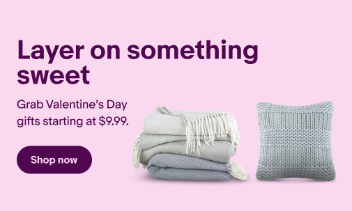 A multi-colored Becky Cameron throw blanket set, arranged in a stack, and a gray Noble House cotton pillow sit against a white background. 