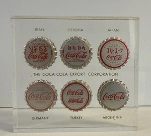 Klar Coca-Cola Export Corporation Briefbeschwerer 6 internationale Cola Flaschenverschlüsse - Bild 1 von 3