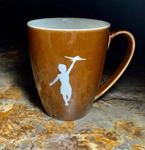 Storyville Coffee Company: Brauner Becher mit Silhouette eines Kindes, das ein Spielzeugflugzeug fliegt - Bild 1 von 7