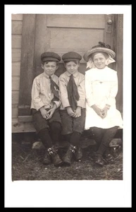 Tres niños sentados por la puerta niños gorras niña sombrero AZO parte posterior dividida foto RPPC - Imagen 1 de 2