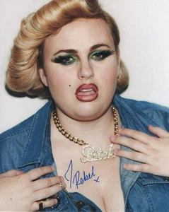 REBEL WILSON SIGNED AUTOGRAPH 8X10 PHOTO - PITCH PERFECT, ISN'T IT ROMANTIC BABE - Picture 1 of 2