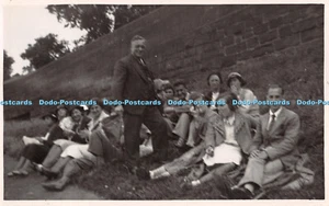 R302869 Women and men sit in the grass Masonry wall Postcard - Picture 1 of 4