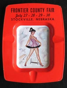 Stockville, NE - 1960s tin litho ASHTRAY - Risque PINUP girlie art - County Fair - Foto 1 di 4