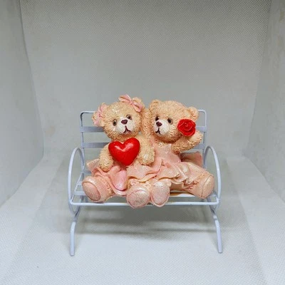 Adorables bailarinas de oso de peluche sentadas en un banco de metal sosteniendo corazón y rosa Foto 1 de 4