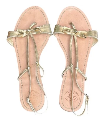 Sandalia plana BCBGeneration para mujer con lazo dorado metálico con tiras Foto 1 de 4