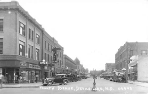Devils Lake ND Fourth Ave. Very Clear Storefronts Old Cars Signage RPPC - Picture 1 of 2