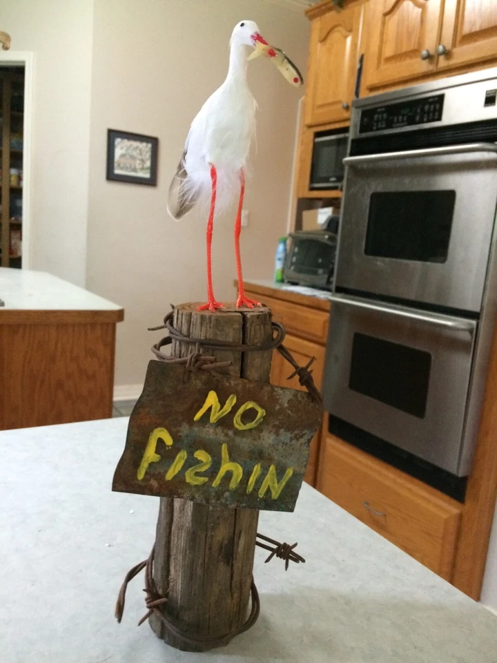 Garceta desafiante en poste de valla con peces.  Artesanía hecha a mano. Foto 1 de 1