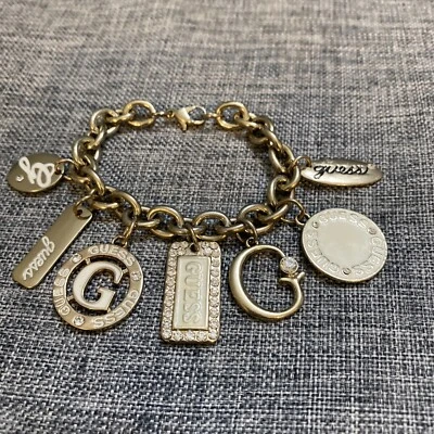 "Brazalete Guess tono dorado metal transparente esmalte blanco varios dijes 7""" Foto 1 de 4